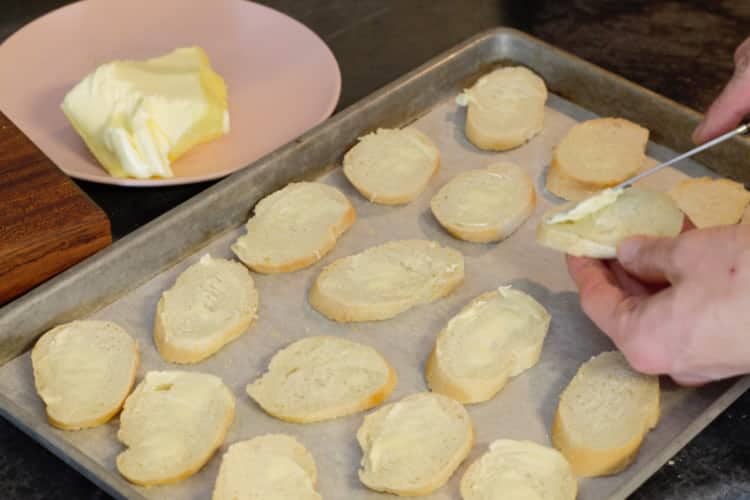 buttering slices of fresh baguette bread and placing them on a sheet pan