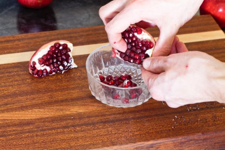 breaking apart pomegranate arils over a small glass dish