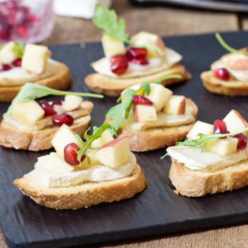 warm brie crostini's topped with a fresh apple and pomegranate salad on a black slate serving board