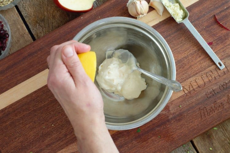 squeezing lemon juice into a metal bowl with mayo