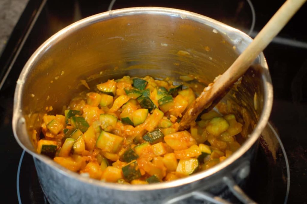 adding curry paste to a pot of cooked mixed veggies