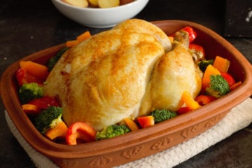 placing mixed bell pepper strips and broccoli florets around a cooked chicken in a clay baker