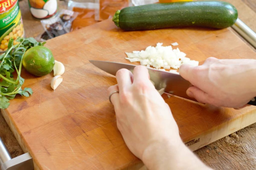 chopping raw white onion on a wooden cutting board