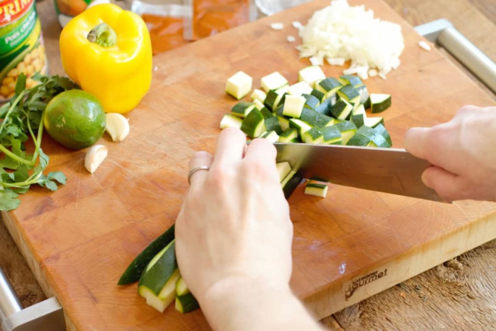 chopping green zucchini on a wooden cutting board