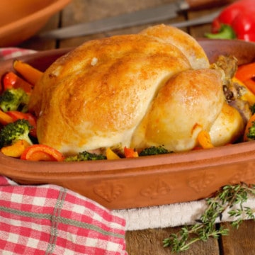 whole roasted chicken in a clay baker surrounded by bell peppers and broccoli