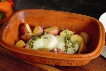 placing potatoes and onions in the clay baker with herbs