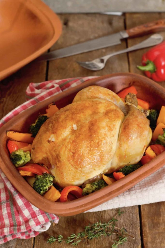 overhead view of the fully cooked whole chicken and vegetables in the clay baker