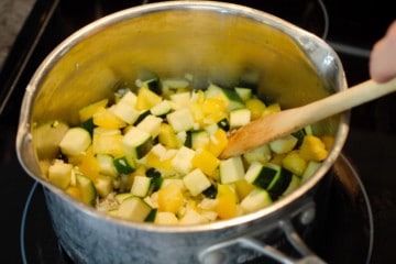 cooking chopped onion,zucchini, bell pepper, and garlic in a pot on the stove