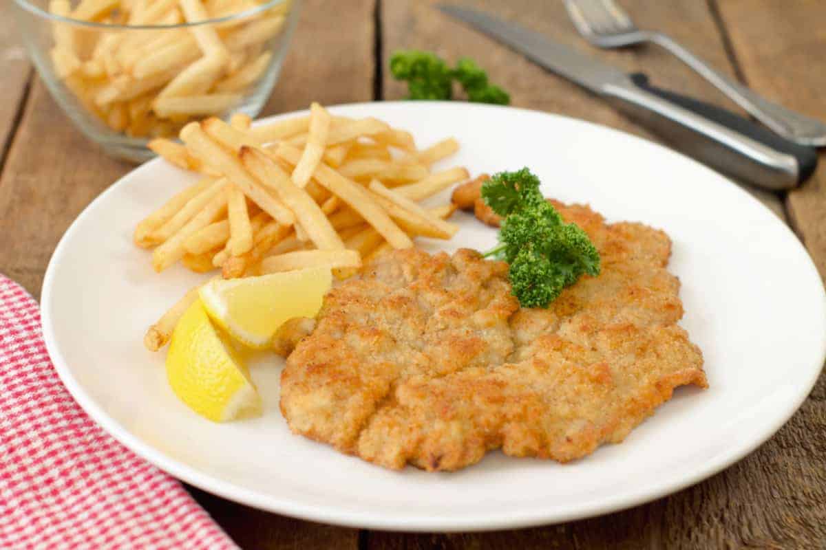 authentic german pork schnitzel served with fries, a wedge of lemon, and parsley on a white plate