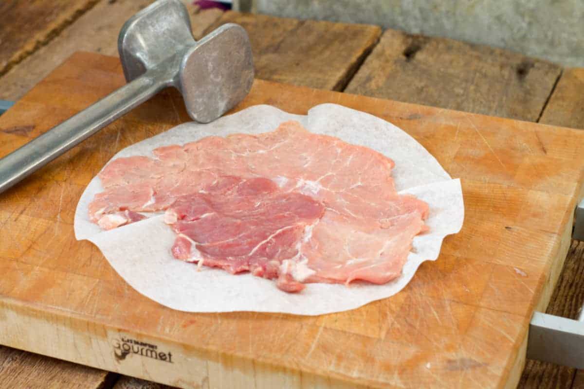 a pounded thin pork cutlet on a wooden cutting board beside a meat mallet for use in making schnitzel