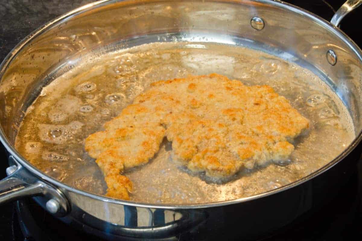 golden brown pork schnitzel being fried in a large pan