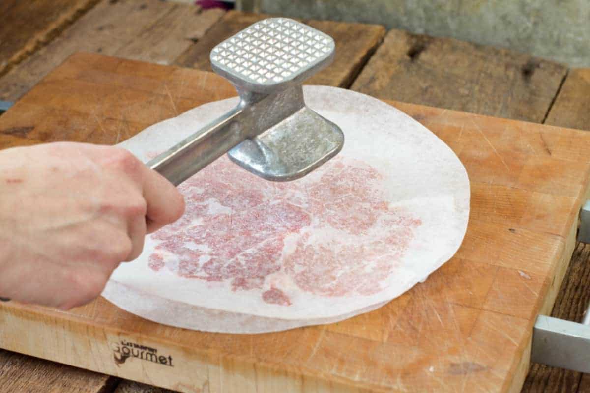 using a meat mallet to pound out a piece of pork between to pieces of parchment