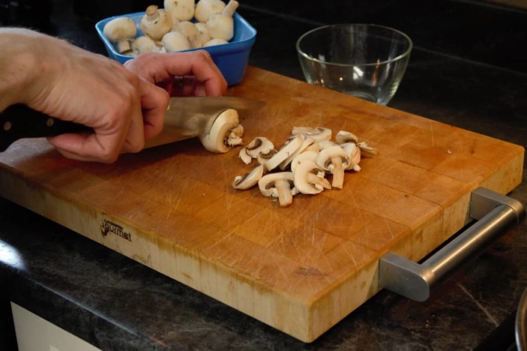 slicing button mushrooms on a wooden cutting board