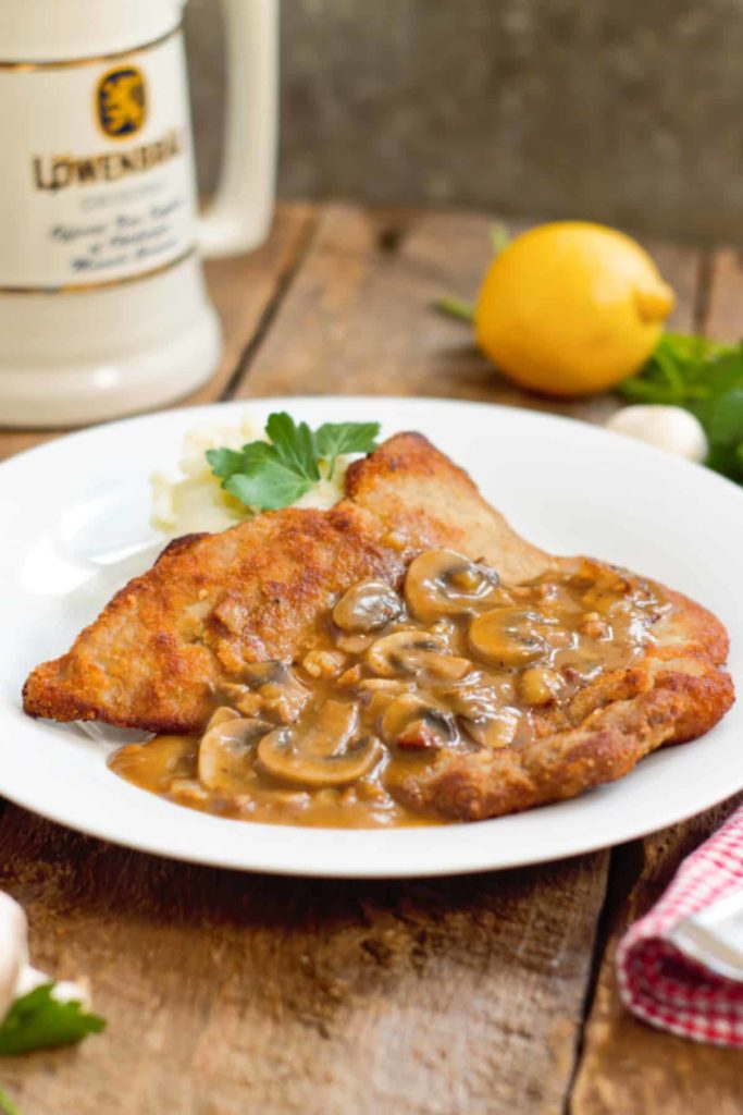 vertical image of a Jägerschnitzel served alongside mashed potatoes on a white plate