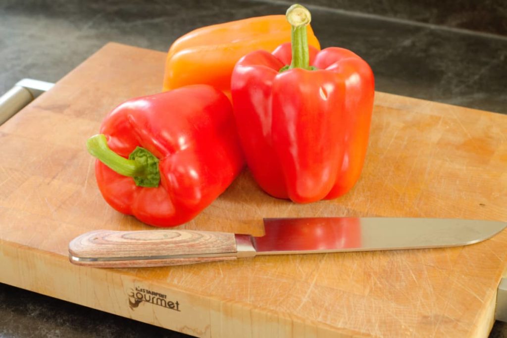 red and orange bell peppers displayed on a wooden cutting board