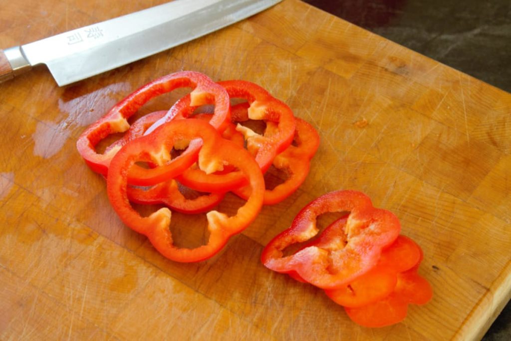 close up of sliced bell pepper rings on a wooden cutting board