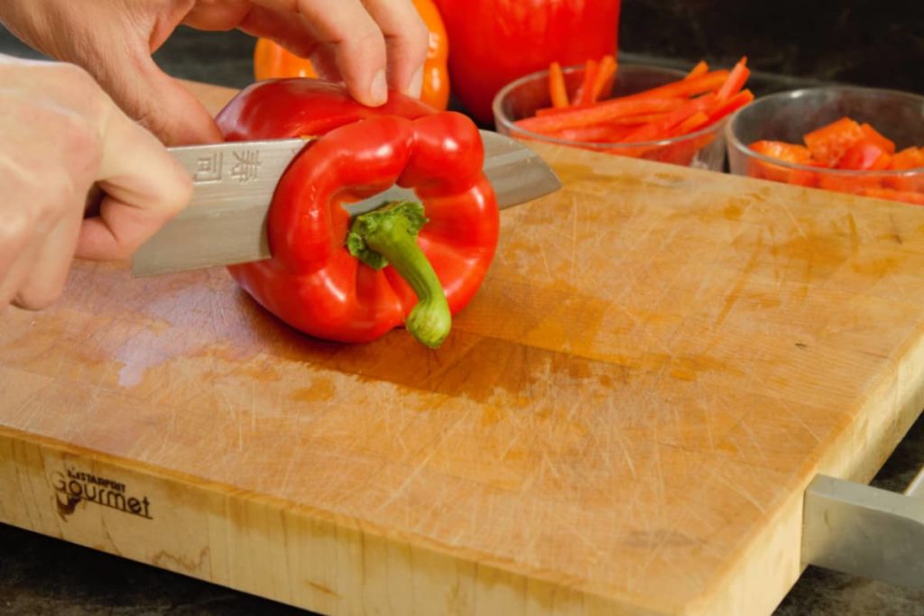 red and orange bell peppers displayed on a wooden cutting board