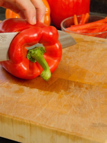 slicing into a red pepper on a wooden cutting board