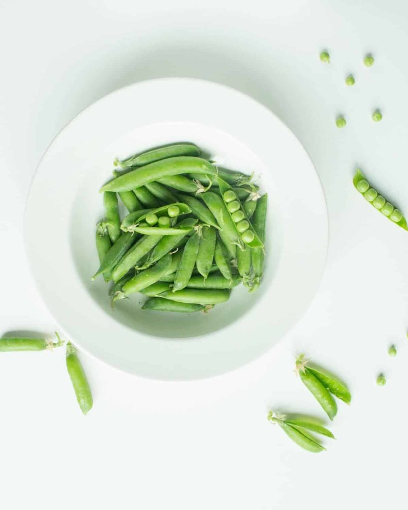 top down shot of peas in a white bowl being shelled