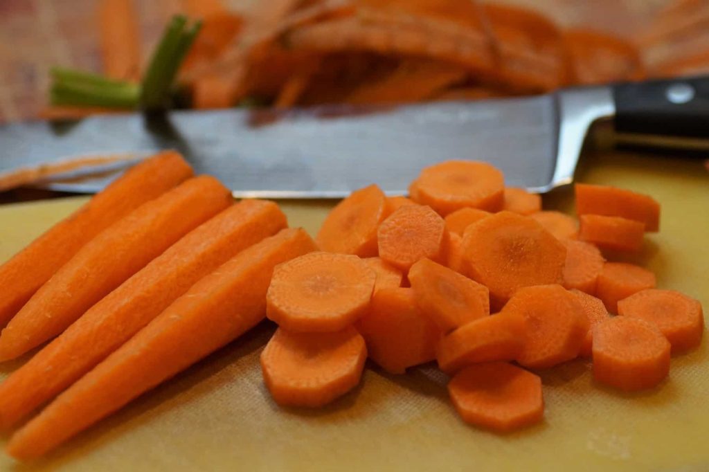 peeled and sliced carrot coin on a cutting board with a chefs knife