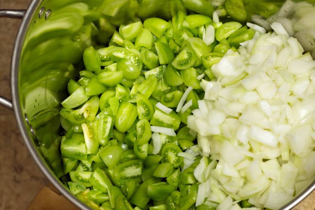 chopped green tomatoes and sliced white onion in a steel pot before mixing