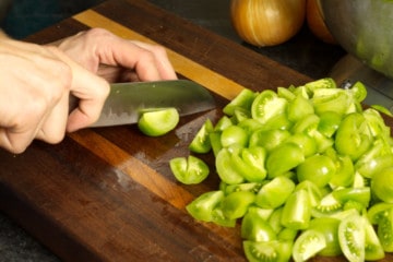 chopping green tomaotes on a wooden cutting board