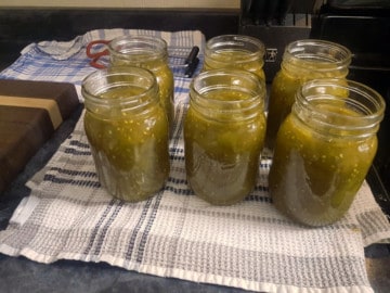 mason jars on a striped dish towel being filled with green tomato chow
