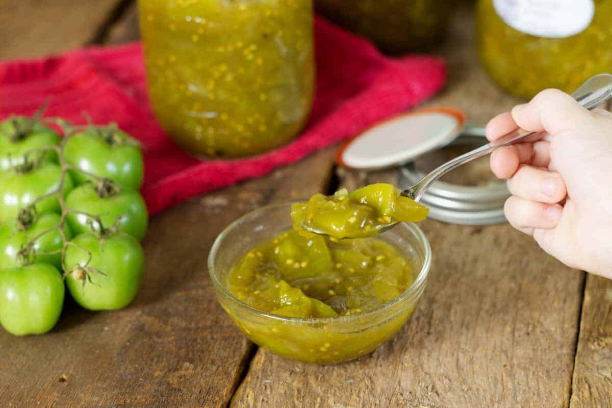 scooping green tomato chow out of a small glass bowl with a spoon