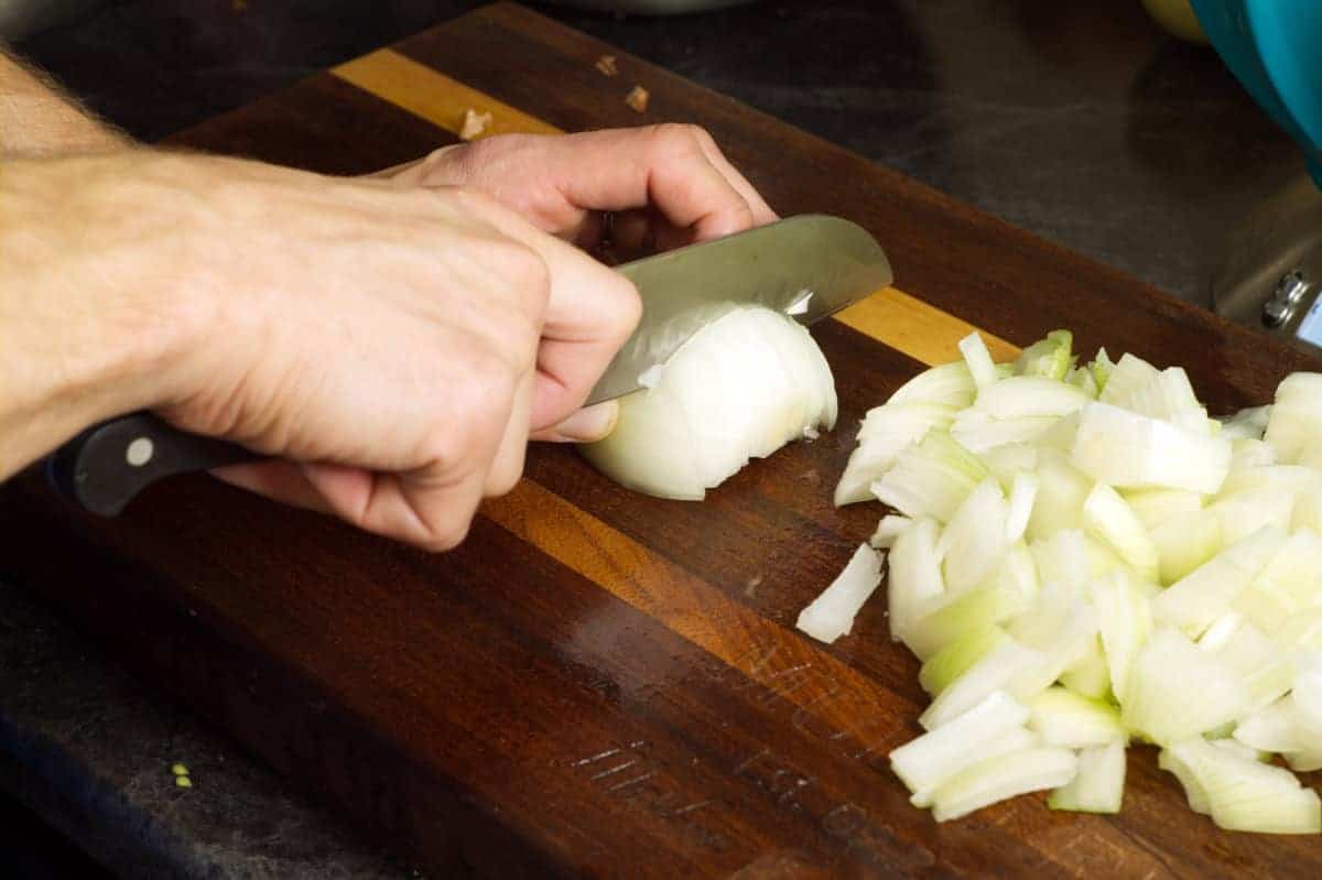 slicing white onion with a chefs knife on a wooden cutting board