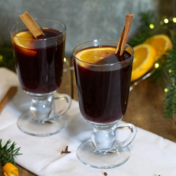 Two glass mugs filled with mulled red wine and garnished with cinnamon sticks and orange.