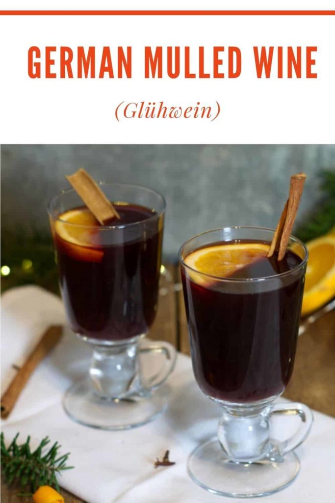 a pinterest image of two glass mugs of german mulled wine on a rustic holiday setting