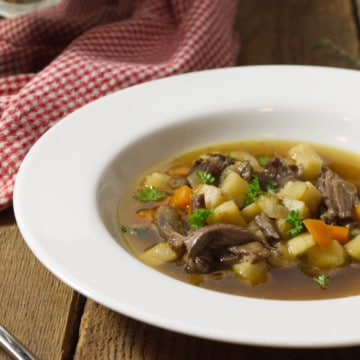 A close up of a white rimmed bowl filled with a broth based oxtail soup, displayed on a barn board background.