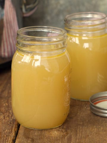 slow cooker turkey stock in glass mason jars on a rustic wood backdrop