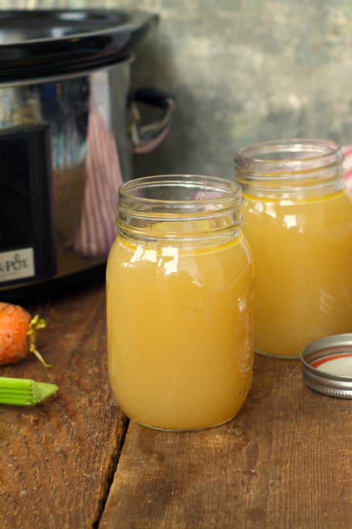 vertical image of slow cooker turkey stock in two mason jars with the slow cooker in the background