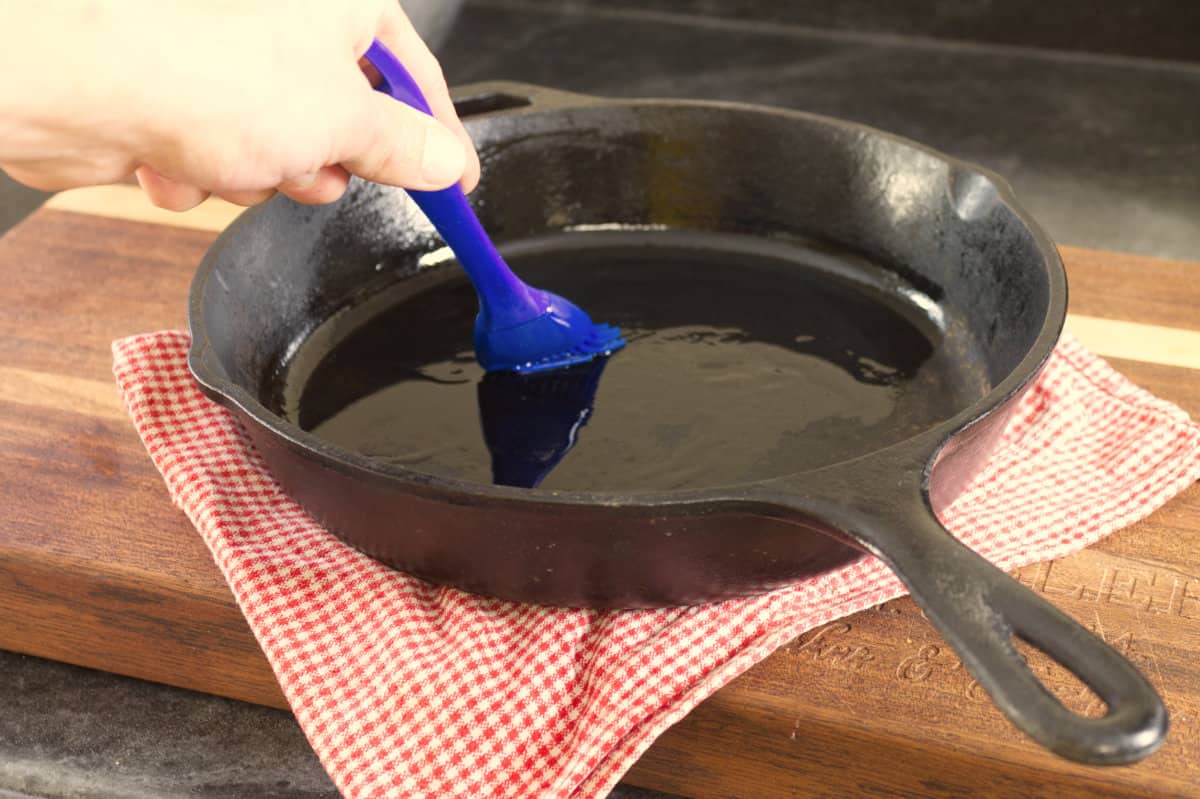 greasing a cast iron skillet with a blue silicone brush
