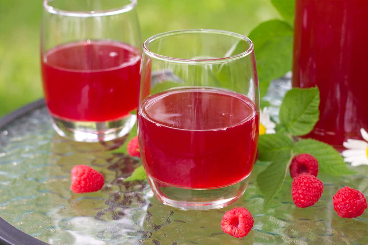close up of a two short glasses of raspberry cordial on a glass table in the garden