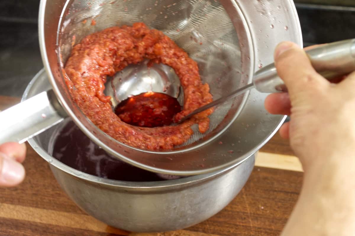 mashing cooked raspberries in a fine mesh strainer to extract as much raspberry juice as possible.