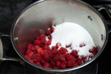 fresh raspberries and white sugar in a large stainless steel pot on the stove.