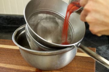 straining cooked raspberries through a fine mesh chinois strainer