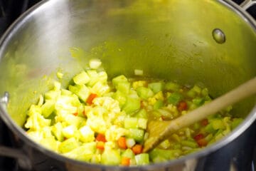 Stirring the prepared mustard pickle vegetables in to the thickened 'spice sauce' with a wooden spoon.