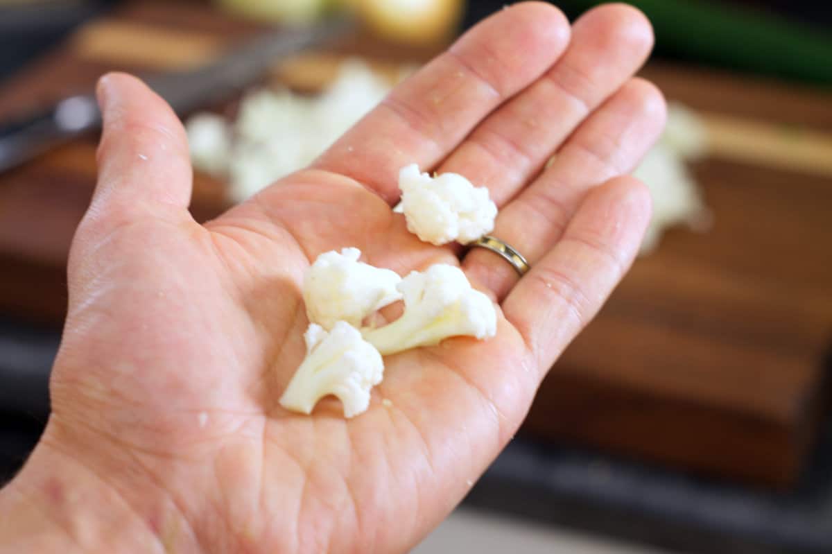 A close-up of a hand holding cauliflower florets to showcase the correct size of cauliflower.
