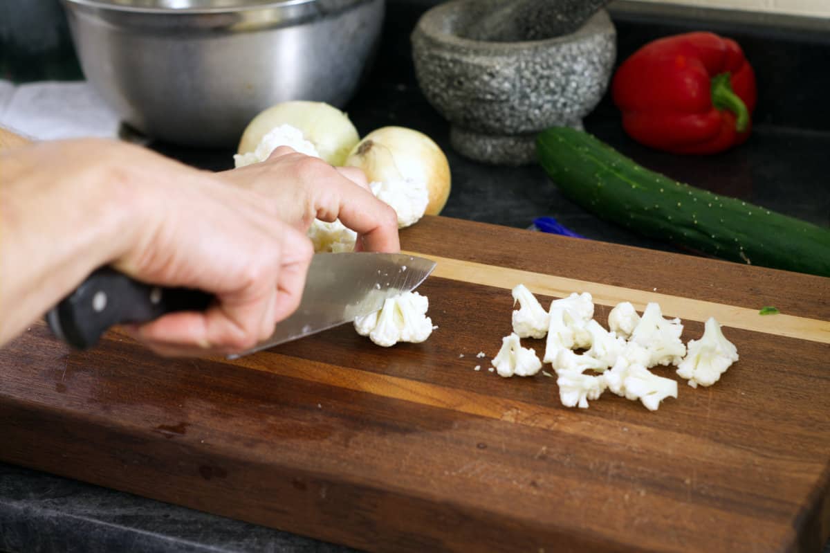 Cutting cauliflower into small bite sized florets on a wooden cutting board.