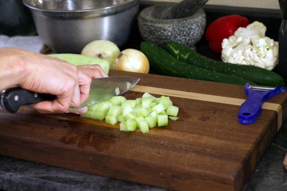 cutting peeled cucumbers into a medium dice cube shape on a wooden cutting board.