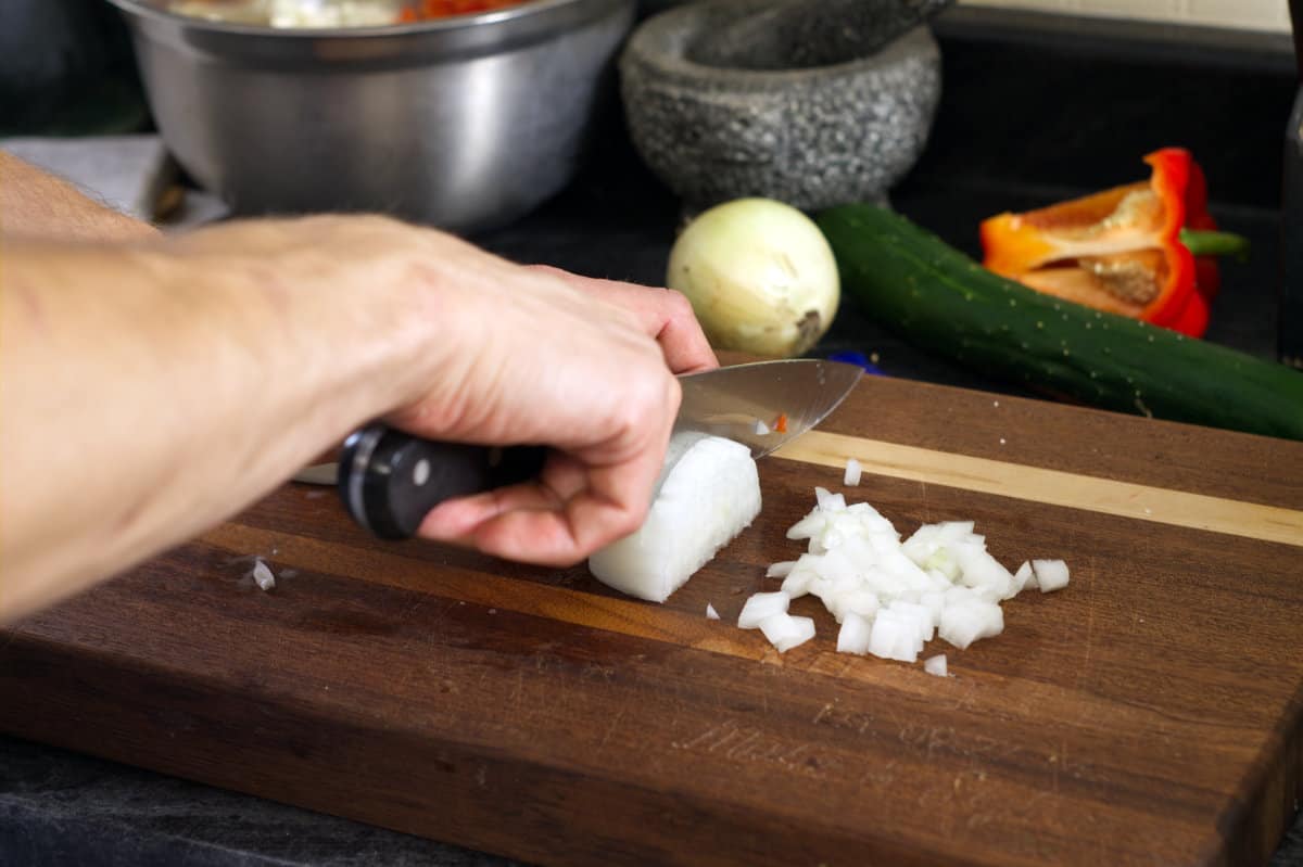 Cutting white onion into a small dice on a wooden cutting board. 