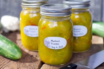 A horizontal image of three jars of fully processed, and labeled mustard pickles displayed on rustic wooden barn boards.