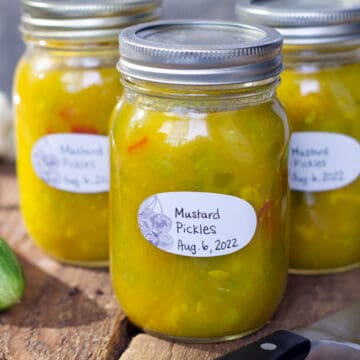 A horizontal image of three jars of fully processed, and labeled mustard pickles displayed on rustic wooden barn boards.