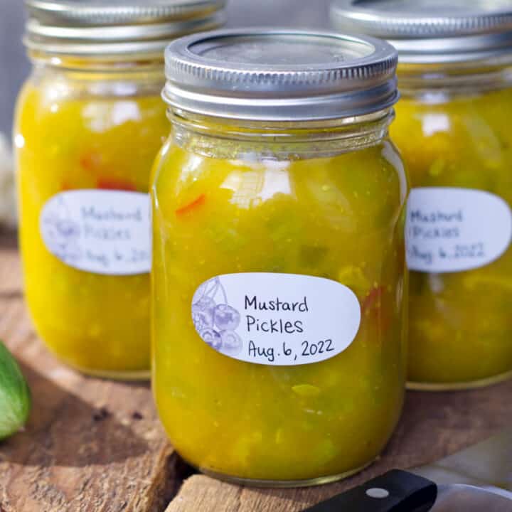 A square image of three jars of fully processed, and labeled mustard pickles displayed on rustic wooden barn boards.