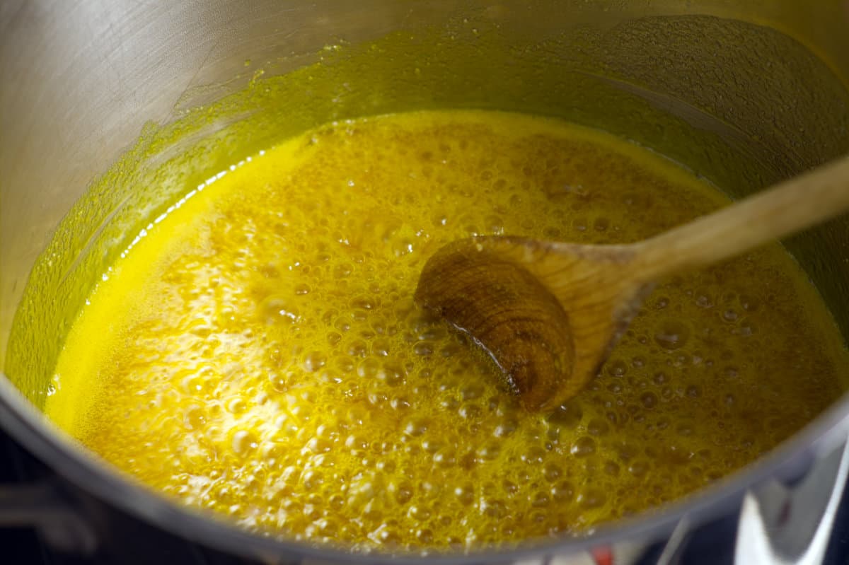 A spice and vinegar mixture simmering in a  stainless steel pot with a wooden spoon stirring the mixture.