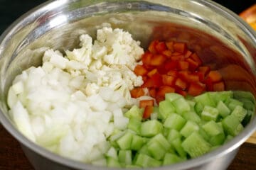 A stainless steel bowl filled with all the prepared vegetables required to make mustard pickles.