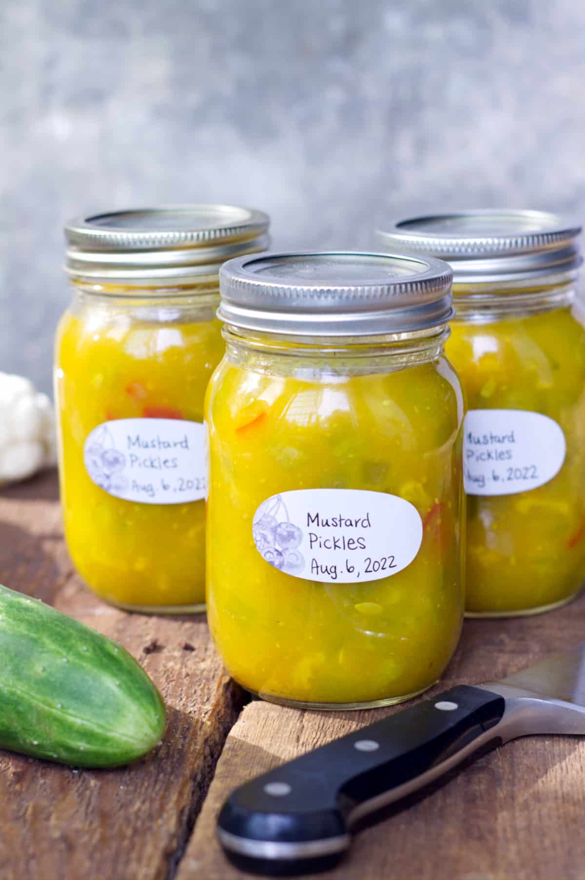 Three jars of fully processed, and labeled mustard pickles displayed on rustic wooden barn boards.